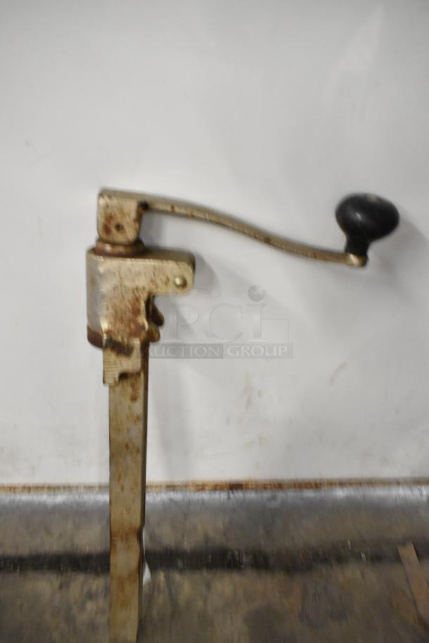 Metal commercial can opener with a long handle and sturdy base, showing signs of wear, suitable for heavy-duty use.