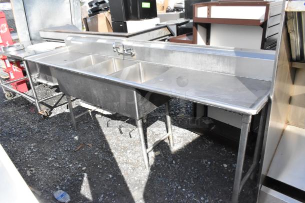 Stainless steel 3 bay sink with dual drain boards, faucet, and handles. Good condition, ideal for commercial use.