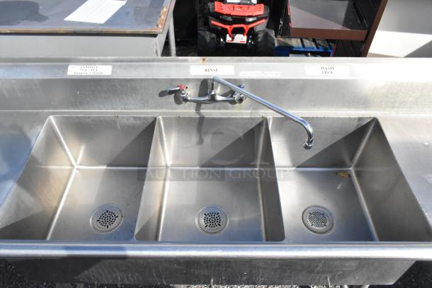 Stainless steel 3 bay sink with dual drain boards, faucet, and handles. Features labeled sanitizer, rinse, wash bins.