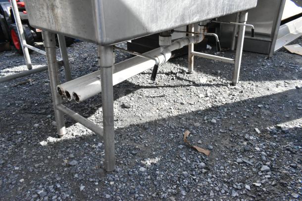 Stainless steel 3 bay sink with dual drain boards, faucet, and handles in used condition. Visible plumbing and sturdy frame.
