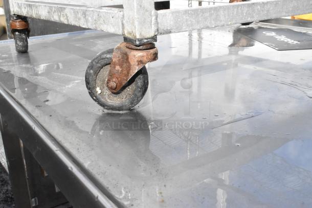 Metal pan transport rack with commercial casters, showing signs of rust and wear. Ideal for industrial kitchen use.