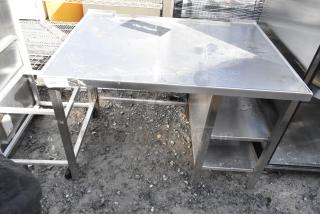 Stainless steel table with under shelves, featuring durable construction and spacious surface. Slight surface wear visible.