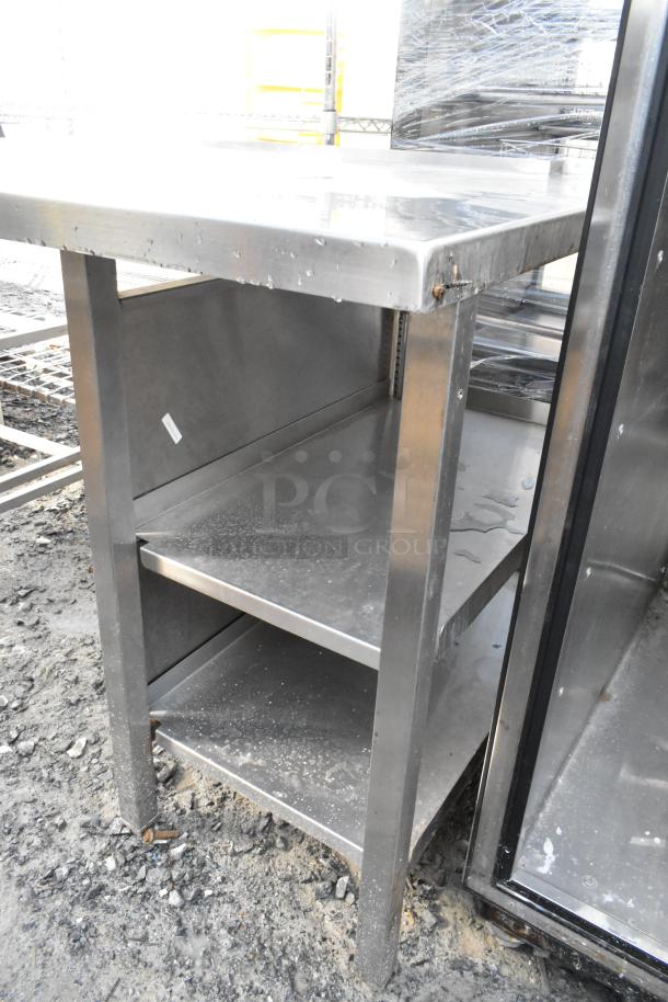 Stainless steel table with under shelves, showing slight wear. Ideal for kitchens or workshops. Durable and functional.