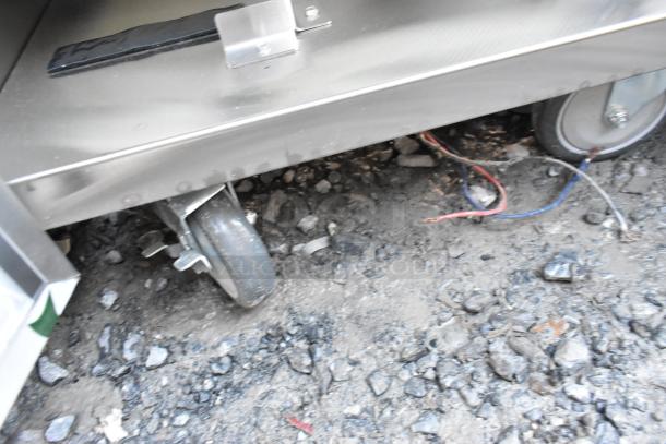 QualServ stainless steel portable sink on casters, scratch and dent condition, showing wheel detail and wiring underneath.
