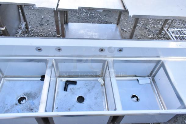 Stainless steel 3-bay sink with dual drain boards, showing scratches. No legs included. Model 600S32424224 by Regency.