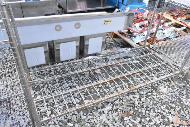 Chrome finish 4 tier wire shelving unit on gravel. Some rust visible. Buyer must dismantle.
