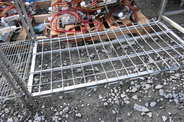 Metro Chrome 5-tier wire shelving unit on rough ground, showing chrome finish, wire grid shelves, dismantling required.