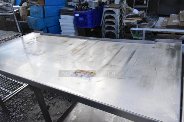 Stainless steel commercial table with under shelf, featuring visible surface wear and a label indicating safety guidelines.