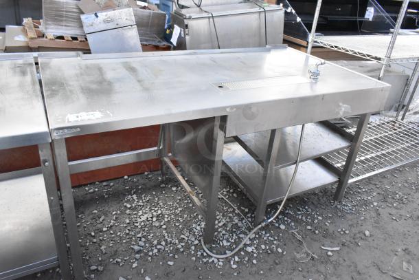 Stainless steel commercial soda station with under shelves, visible wear. Includes faucet and drainage area.