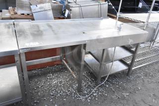 Stainless steel commercial soda station with under shelves, visible wear. Includes faucet and drainage area.