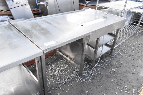 "Stainless steel commercial soda station with under shelves, durable construction, slight wear, labels visible, spacious."