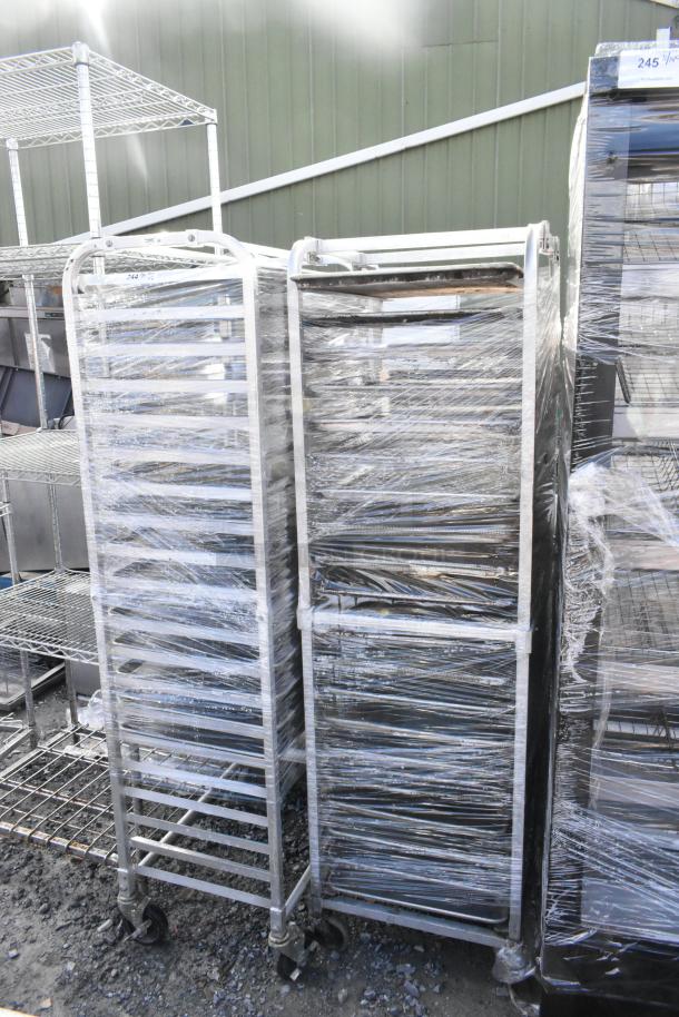 Two metal commercial pan transport racks with baking pans, wrapped in plastic, featuring sturdy wheels for easy mobility.