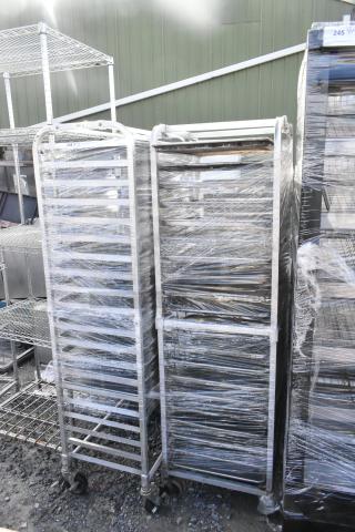 Two metal commercial pan transport racks with baking pans, wrapped in plastic, featuring sturdy wheels for easy mobility.