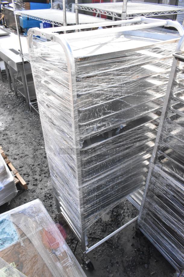 Two metal commercial pan transport racks with multiple baking pans, wrapped in plastic. Includes wheels for mobility.