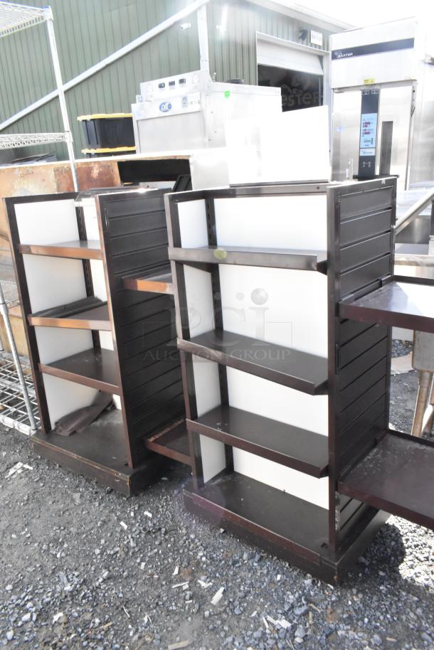 Two metal merchandising display racks, dark finish, each with four adjustable shelves, in used condition.
