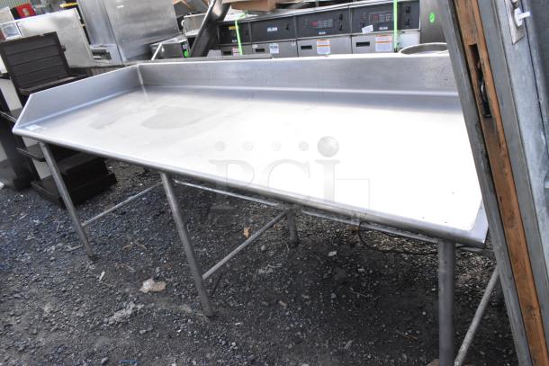 Stainless steel table with high back splash, sturdy legs, and used condition visible outdoors. Ideal for industrial use.