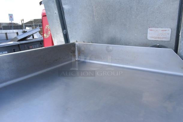Stainless steel table with backsplash, gently used condition, visible label indicating care instructions.