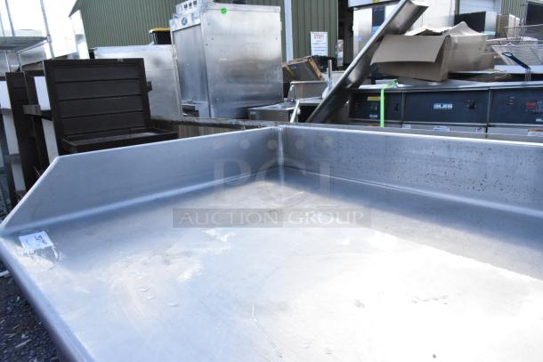 Stainless steel table with raised edges, pre-owned, visible surface wear. Industrial setting with surrounding equipment.