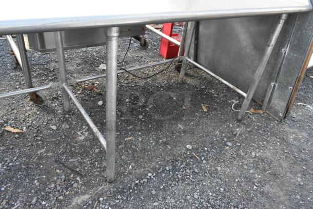 Stainless steel table with sturdy legs and a smooth surface, showing signs of outdoor wear. Ideal for industrial use.
