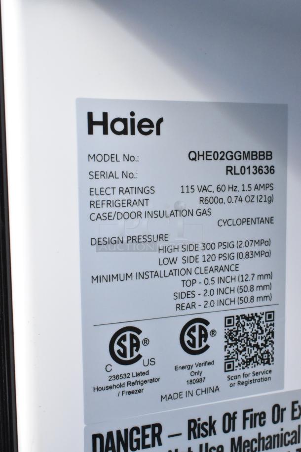 Label close-up for Haier QHE02GGMBBB cooler, showing specs: 115VAC, R600a refrigerant, design pressure, and clearance details.