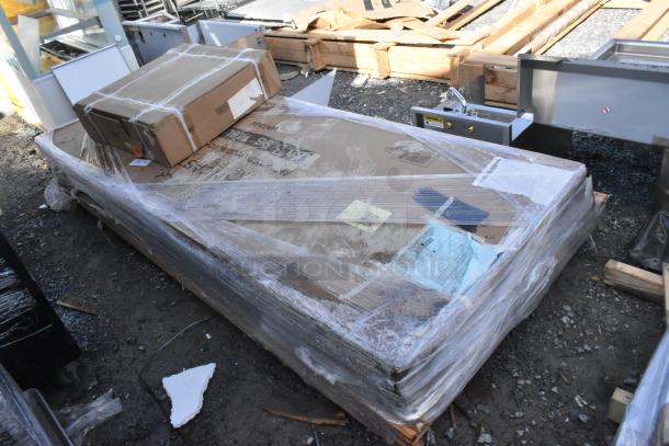 Four brand new scratch and dent items wrapped on a pallet, including Regency drawer and Lancaster table tops.