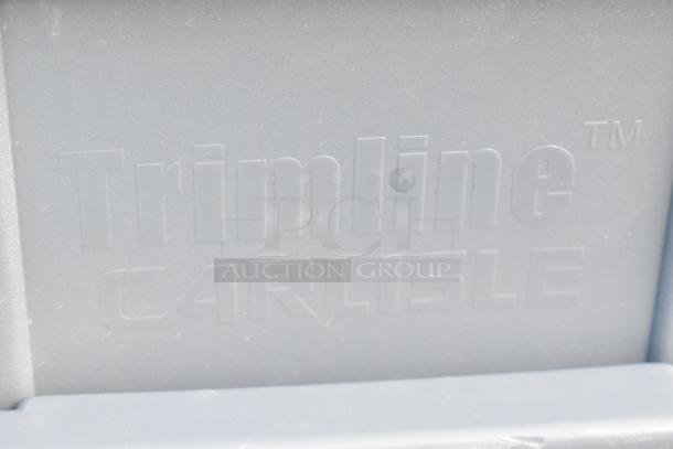 Close-up of Trimline Carlisle logo on a gray plastic surface, part of the auction item including Orbis black poly bins.