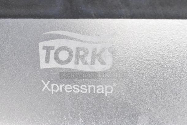 Close-up of a surface with "Tork Xpressnap" logo embossed, indicating a connection to the gray poly trash can product.