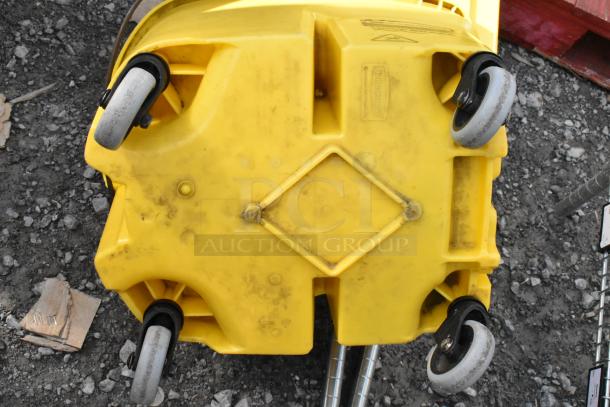 Yellow poly mop bucket with wringing attachment, visible scuffs and dirt, sturdy wheels for mobility.