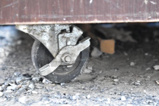 Commercial caster of trash can shell with deposit holes and doors, shown against a gravel ground, indicating mobility.