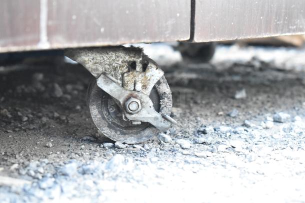 Trash can shell with deposit holes and doors on commercial casters, metal construction, visible wear and dirt on wheels.