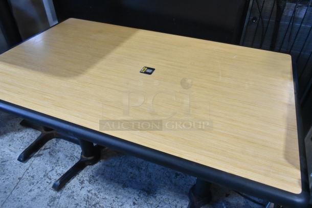 Wood-pattern dining table with black metal bases, features a smooth surface, and a small visible label; in good condition.