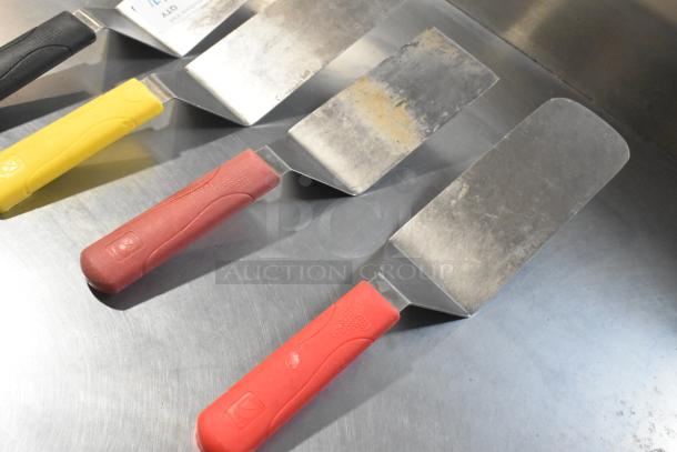 4 metal spatulas with color-coded handles in red, yellow, and black. Used condition; some surface wear visible.