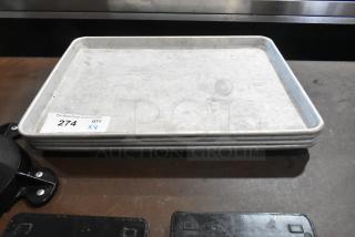 4 stacked metal half-size baking pans, lightly worn, with auction label "274 QTY x4." Suitable for baking needs.