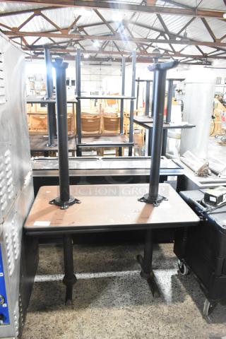 Two wood-pattern dining tables with black metal legs, stacked upside down. Excellent condition. Auction item.