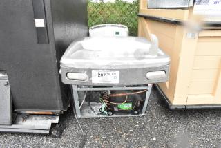 Metal wall mount water fountain with visible piping and wiring beneath. Auction tag indicates quantity: 2. Slight wear.