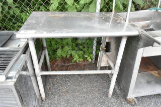 Stainless steel table with sturdy tubular legs, showing surface wear. Suitable for kitchen or industrial use.