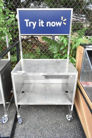 Stainless steel cart with under shelf, on commercial casters. "Try it now" sign attached. Some visible surface wear.