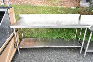 Stainless steel table with backsplash and under shelf, outdoor setting, good condition, visible label on side.
