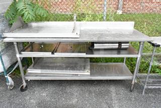Stainless steel table with two under shelves on commercial casters, featuring a backsplash and durable construction, outdoor setting.