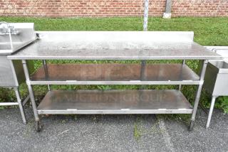 Stainless steel table with two under shelves on commercial casters, weathered condition, ideal for commercial use.
