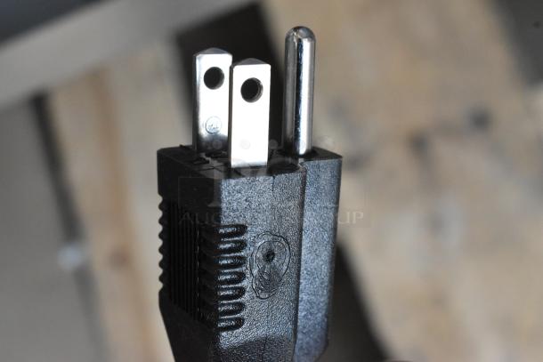 Close-up of a three-prong electrical plug, showing a polarized blade and safety certification mark. The plug is black with textured grip.