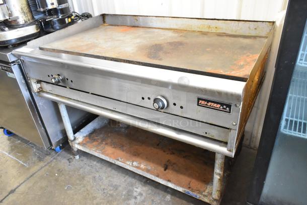 Tri-Star Stainless Steel Commercial Flat Top Griddle on equipment stand, used condition, with visible rust and control knob.