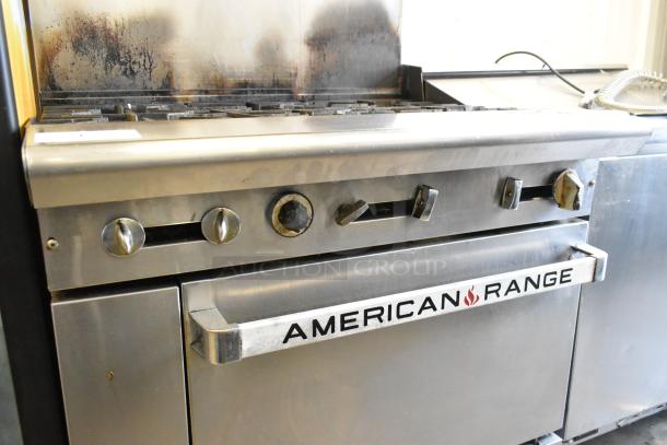 American Range stainless steel 6-burner gas range with salamander, backsplash, and oven. Visible wear, ideal for commercial use.