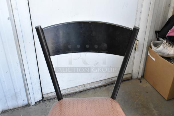 Dining chair with curved black backrest and orange-brown seat cushion. Rustic condition. 7 chairs available per bid.