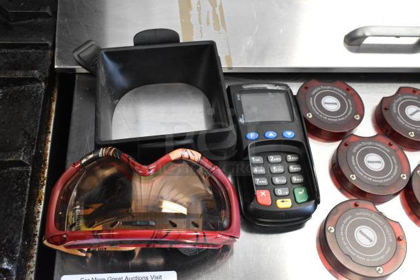 Lot with 2 credit card readers, 6 queuing wireless call discs, a hard drive, and goggles. Items on metal surface.