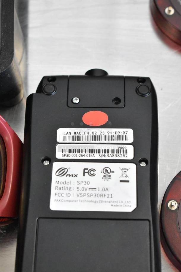 Alt text: PAX SP30 credit card reader with visible label showing model, rating, and FCC ID details alongside queuing disc.