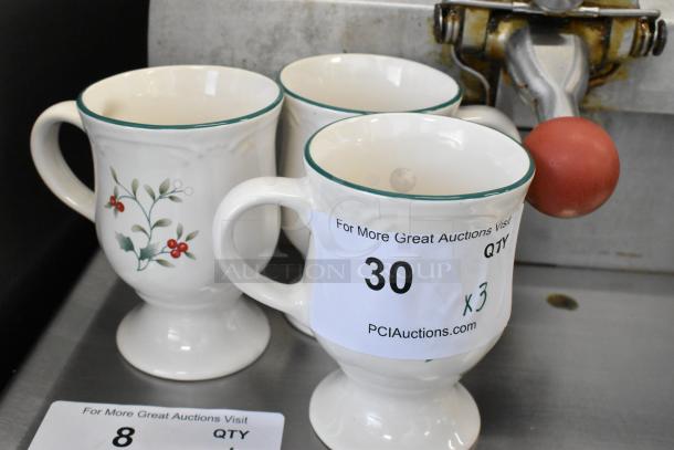 Three white ceramic footed mugs with green rim and holly design, marked “30 x 3” for auction quantity.
