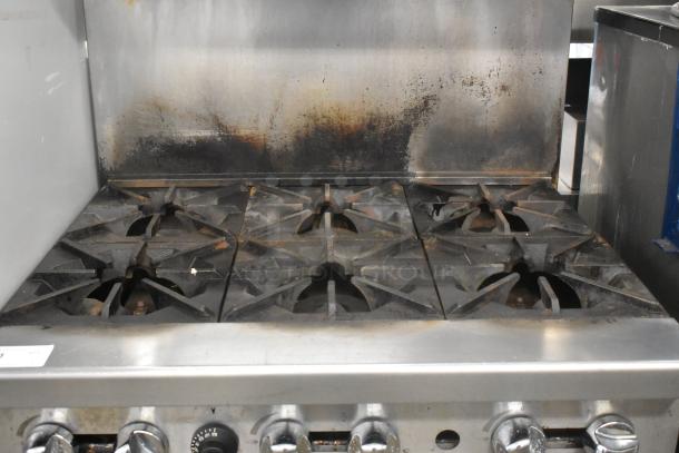 Cookrite stainless steel 6 burner gas range with oven, over shelf, backsplash, and commercial casters. Used condition.
