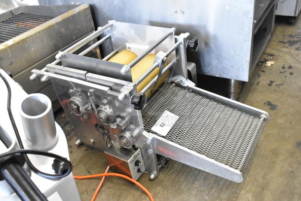 Metal countertop sheeter with adjustable rollers, sturdy frame, and stainless steel conveyor. Visible tag reads "62."