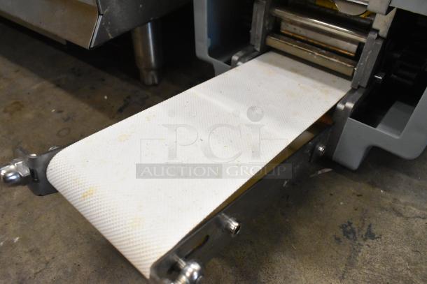 Metal commercial countertop sheeter with white textured conveyor, in used condition, visible slight discoloration.